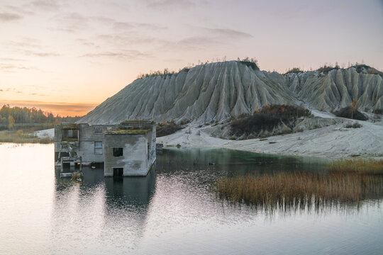 View of submerged building ruins reflecting in the still waters against a backdrop of textured sand hills under a soft, pastel sky, Rummu, Harju maakond, Estonia.