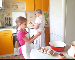 A grandmother and her granddaughter set out the necessary ingredients for cooking on the table.