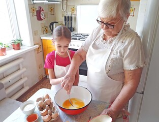 A grandmother and her granddaughter are making pancakes in the kitchen.