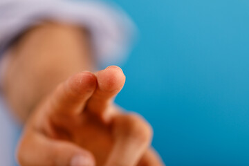 Obraz premium Human hand pointing, gesture of choosing, focus or selecting. Blue backdrop with soft focus in the background. Concept of direction, decision, a