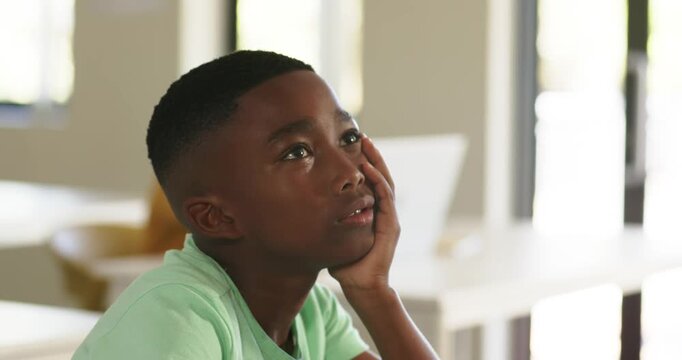 African American child in green tee seeing offscreen leaning resting cheek on right hand in class