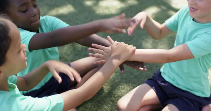 Female children placing hands together, stacking and shuffling on green turf, playing team game