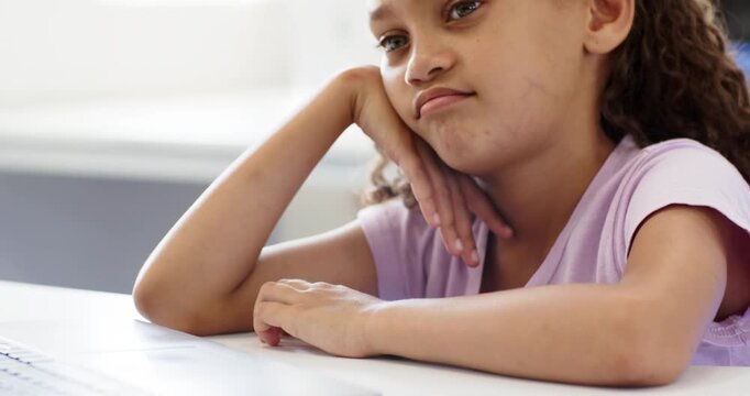 Camera zooming in, African American child at desk, shirt, resting head on hand, studying on laptop
