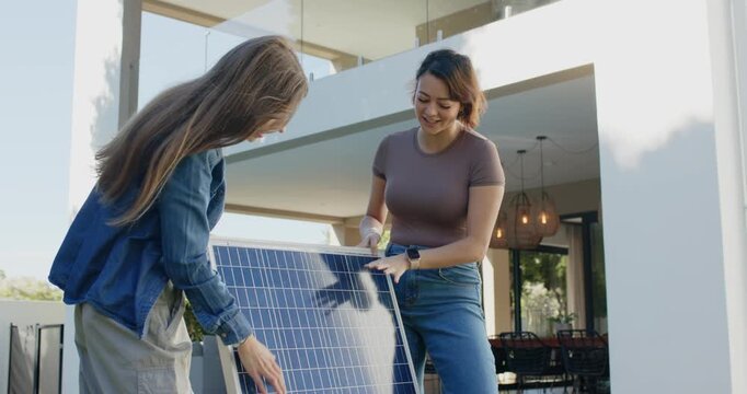 Two women lifting solar panel upright from ground on patio, adjusting grips and installing