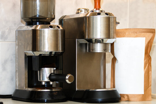 Industrial style coffee maker and burr grinder with blank coffee bag on marble surface. Minimalist kitchen appliance mockup for coffee branding and packaging design