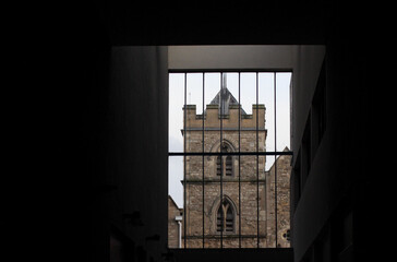 The stone tower of St Ebbe's Church in Oxford, framed by the dark interior and grid-like bars of a modern adjacent building of the Westgate Centre.