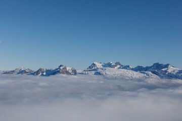 Dramatic landscape of snow-capped mountains peaking above clouds against a clear blue sky. Nature's