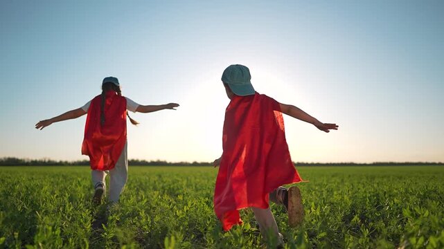 Superhero cape flow behind boy and girl. Children play on wide field running fast. Outdoor summer joy children laughing. Boy girl in superhero cape love running. Happy children keep playing outside.