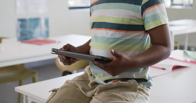 Child shifting after tapping tablet and leaning forward, holding tablet for learning in classroom