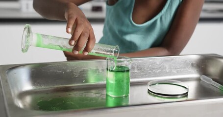 Child is tilting cylinder, pouring green liquid into beaker on tray making foam overflow for demo - Powered by Adobe