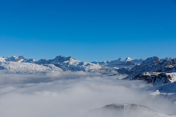Stunning landscape of snow-capped mountains peaking through clouds under a clear blue sky. A beautif