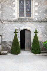 Historic Stone Church Entrance With Arched Doorway, Stained Glass Window, and Twin Topiary Crosses