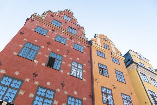 View of vibrant, sun-drenched facades of historic buildings ascend towards the sky, a fusion of red, orange, and yellow hues in Stortorget, Stockholm, Sweden.