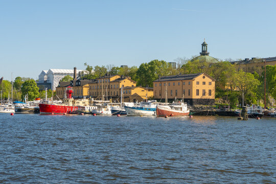 View of boats bob gently in the shimmering waters, framed by the ochre buildings and verdant trees under a clear sky, Stockholm, Stockholm County, Sweden.