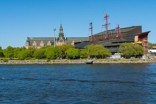 View of the Nordic Museum's intricate architecture with Vasa Museum, under a clear blue sky, reflected in the water, Stockholm, Stockholm, Sweden.