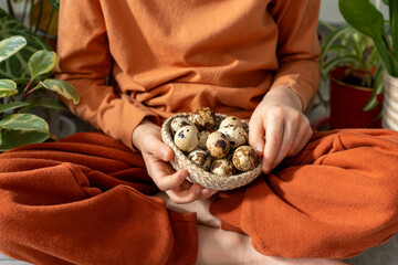 Both hands of a boy holding a braided bowl of quail eggs, dressed in brown clothes.