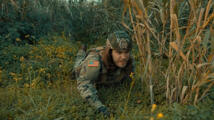 A soldier crawls on the ground in a meadow to better observe the enemy