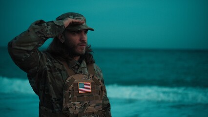 On a beach, an American soldier salutes near the ocean During Veterans Day