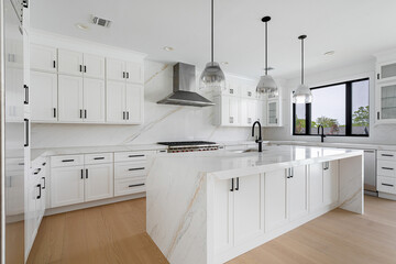 Bright modern white kitchen with large marble island and pendant lighting, luxury residential kitchen interior with minimalist contemporary design © nagelsphoto