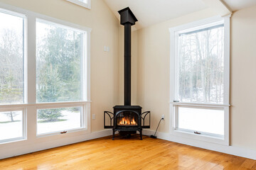 Obraz premium Cozy living room with black wood burning stove and large windows, warm minimalist home interior with winter forest view and natural light