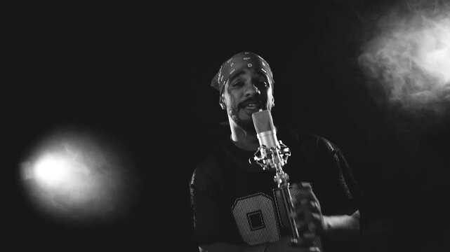 Black and white scene of a talented male rapper passionately singing into a vintage microphone. Smoky, dark background with spotlights