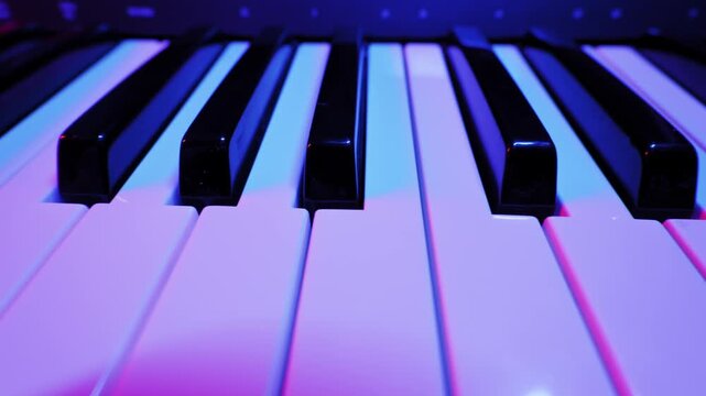Black and white piano keys of a synthesizer slide slowly across the frame. Moody purple and blue stage lights create vibrant reflections on the glossy surfaces.