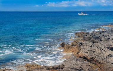 sea view from rocky coast with a beautiful blue water and a fishing boat in the distance in   Peloponnese in Greece