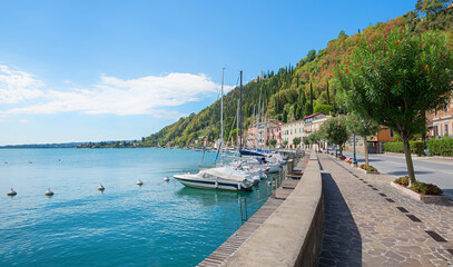 Fototapeta premium pictorial lakeside promenade Maderno, lake Gardasee, moored sailboats