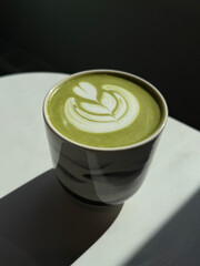 Cup of matcha latte in a sunbeam on the table. Tasty trendy drink concept. Handmade smartphone photo, selective focus, harsh sunlight, non AI