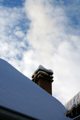 Brick chimney on a snow-covered roof against a cloudy winter sky