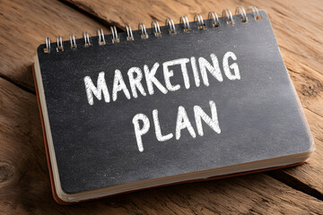 Notebook shows marketing plan written in simple white letters on dark background placed on wood table at office
