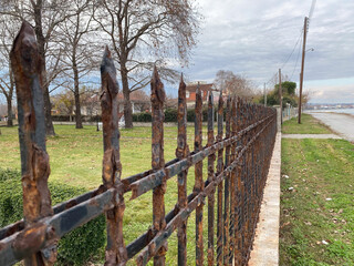 Rusty iron fence lining leafy park path with overcast sky background