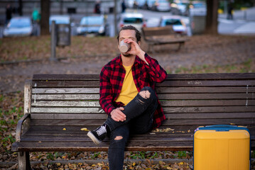 Tourist with a rolling suitcase drinking coffee in a park
