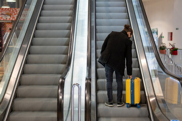 Man with face mask at the airport with a rolling suitcase on escalator
