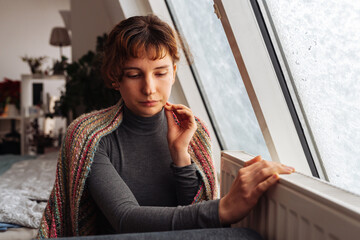 young woman warms herself near radiator at home in winter weather.