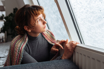 young woman warms herself near radiator at home in winter weather.