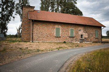 Ein altes Backsteingeb&auml;ude mit gr&uuml;nen Fensterl&auml;den steht ruhig in l&auml;ndlicher Umgebung