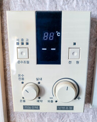 Close-up of old analog gas boiler heating controller on the wall in Korea. Korean text interface with dial and buttons. Concept for winter heating costs and Ondol system. © Eunyoung