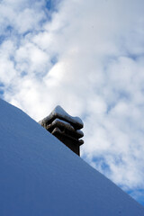 Brick chimney on a snow-covered roof against a cloudy winter sky