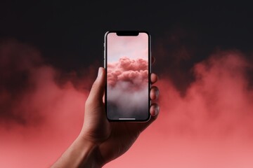 Hand holding a modern smartphone with a surreal pink sky and clouds background