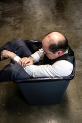 Failed Businessman Stuffed into Trash Can. Concept of Being Sacked or Fired. Victim of Stock Market Crash.