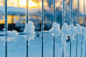 Close-up of hoarfrost-covered fence glowing in golden sunset light, revealing detailed ice crystals and frozen metal textures. selective focus, atmospheric lighting themes.
