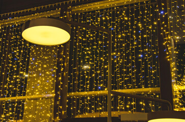 street lamp in front of a building facade decorated with warm yellow fairy lights at night. Urban outdoor lighting creating a festive atmosphere in the city environment.