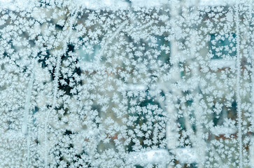 Delicate frost crystals form intricate snowflake patterns across icy window pane in cool blue tones, ideal for winter holiday backgrounds or elegant seasonal branding with space for text