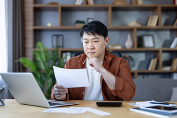 Fototapeta premium Man checking bills and preparing taxes at his home office, analyzing financial documents and using a laptop and calculator for budgeting and debt management