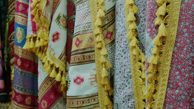 Richly patterned traditional bosnian textiles hanging side by side in market stall. Fabrics feature geometric motifs, floral elements and bright tassels, highlighting artisanal balkan craftsmanship