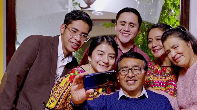 A Mayan family takes a photo during a celebratory dinner. The family smiles at the smartphone camera.