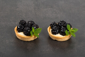 Two blackberry round tartlets. Decorated with mint. Dark gray background. Close up	