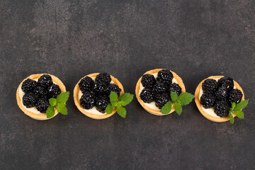 Blackberry round tartlet. Decorated with mint. Dark gray background. Top view	
