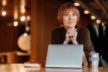 Thoughtful woman in her 40s working on laptop at table in modern interior